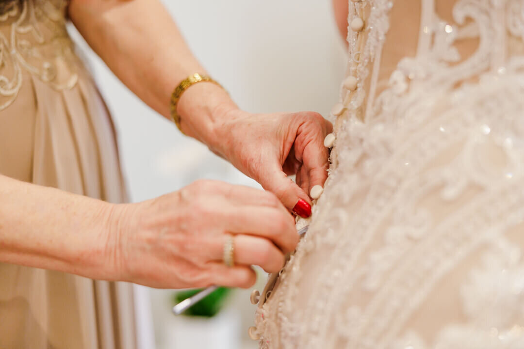 A close up of mom buttoning up the back of a brides dress. Captured at The Venue at Oakdale in North Little Rock, AR.