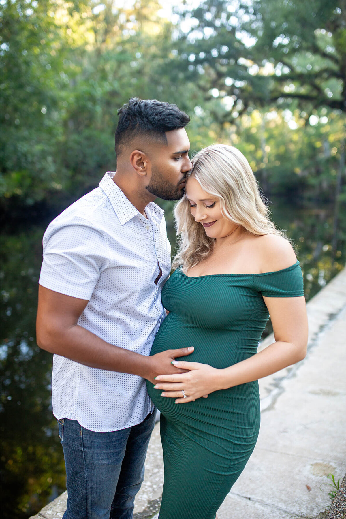 Man kissing blond pregnant mother by the river while holding belly