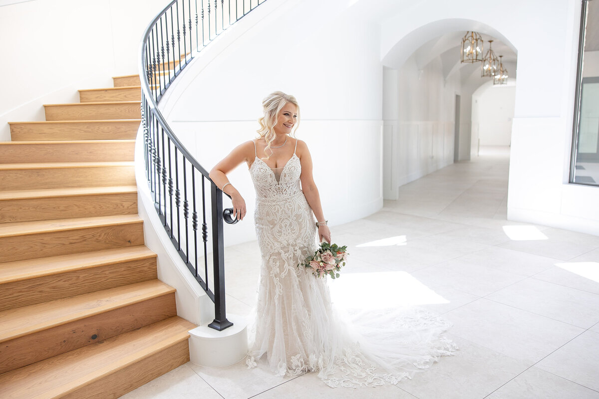 bride leans agains spiral staircase at The Preserve at Canyon Lake Texas wedding  white walls French light fixtures