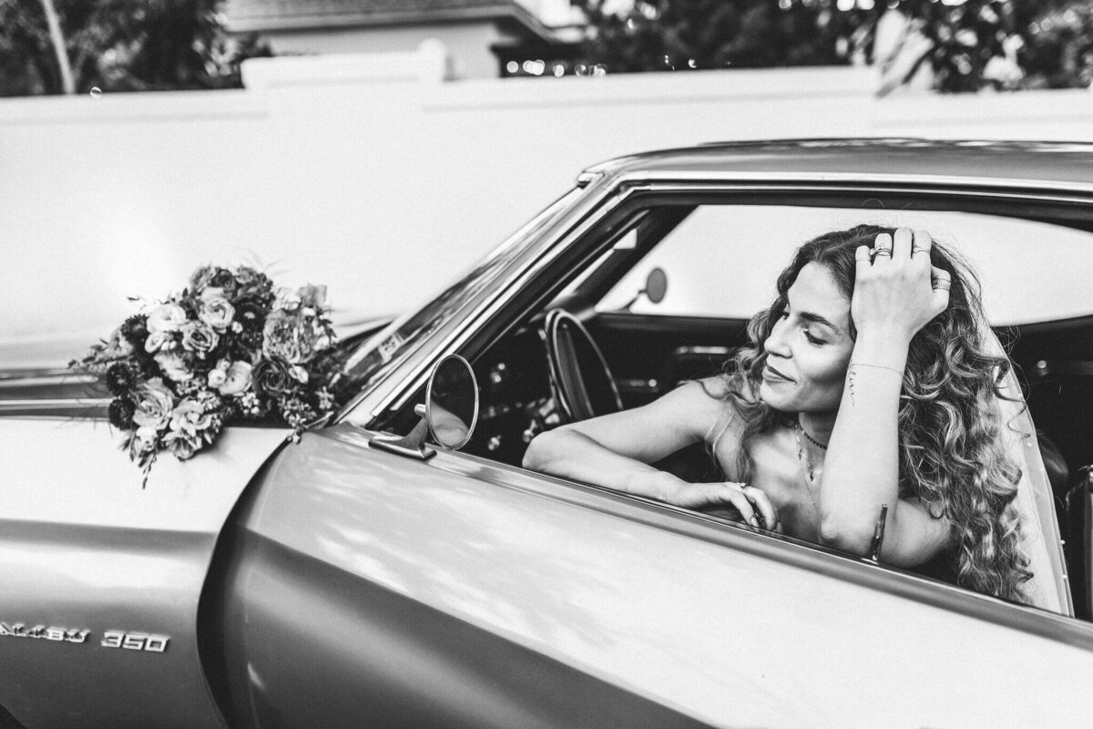 black and white photograph of bride in vintage car with bouquet on car at East Texas wedding venue