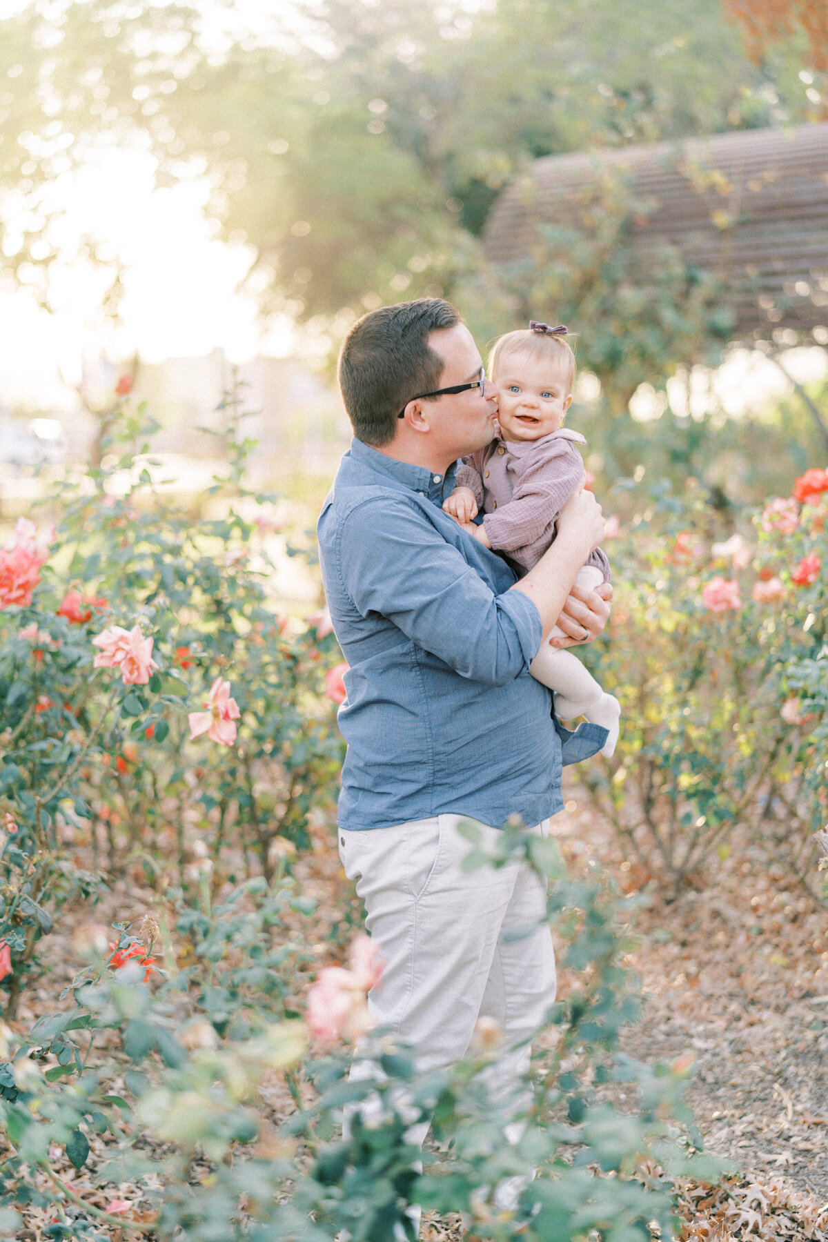 dad in blue shirt holding little girl in purple giving her a kiss on the cheek