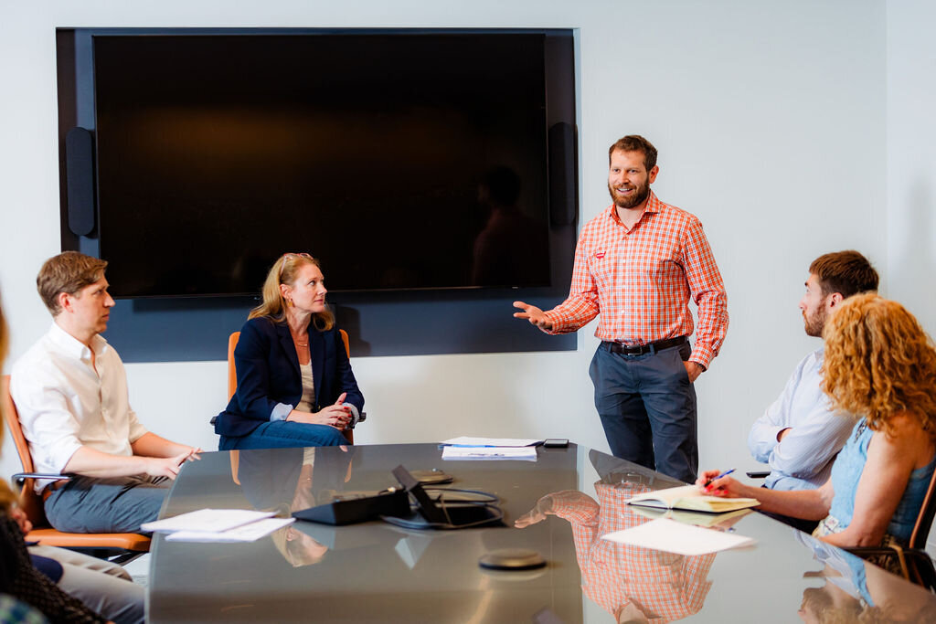 People sit around a table listening to a presenter.