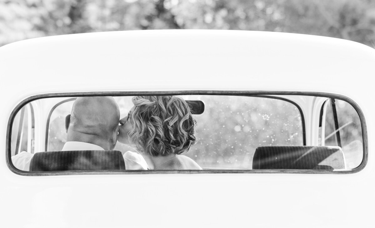 Wife kissing her husband through the back window of a white vintage truck for couple’s photos.