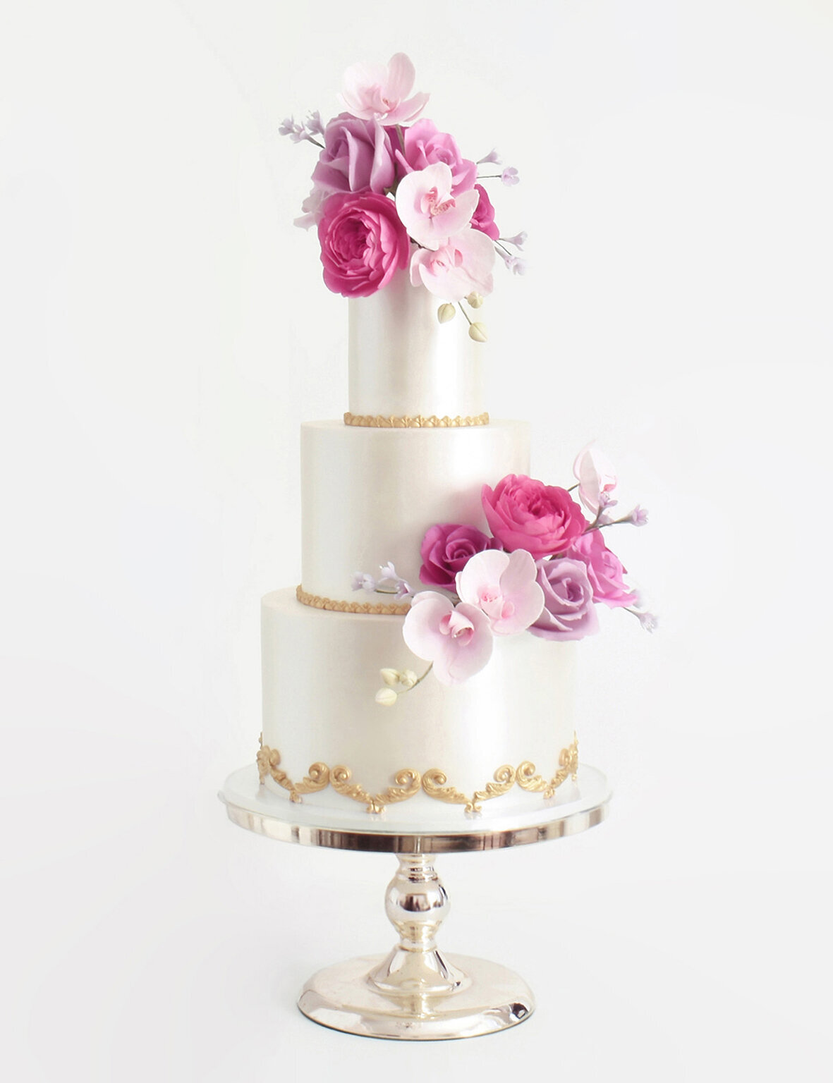 A Glamorous three tiered wedding cake with gold baroque detail and vibrant pink and purple sugar roses and orchids
