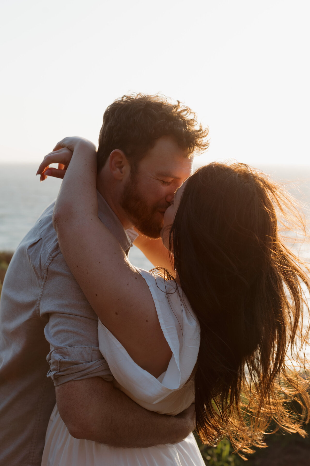 A couple shares a passionate kiss at sunset by the ocean, capturing intimate and cinematic wedding photography.