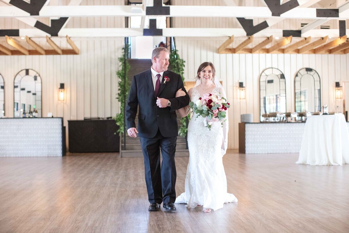 bride's father looks down at her as they walk toward indoor ceremony at Milestone New Braunfels wedding