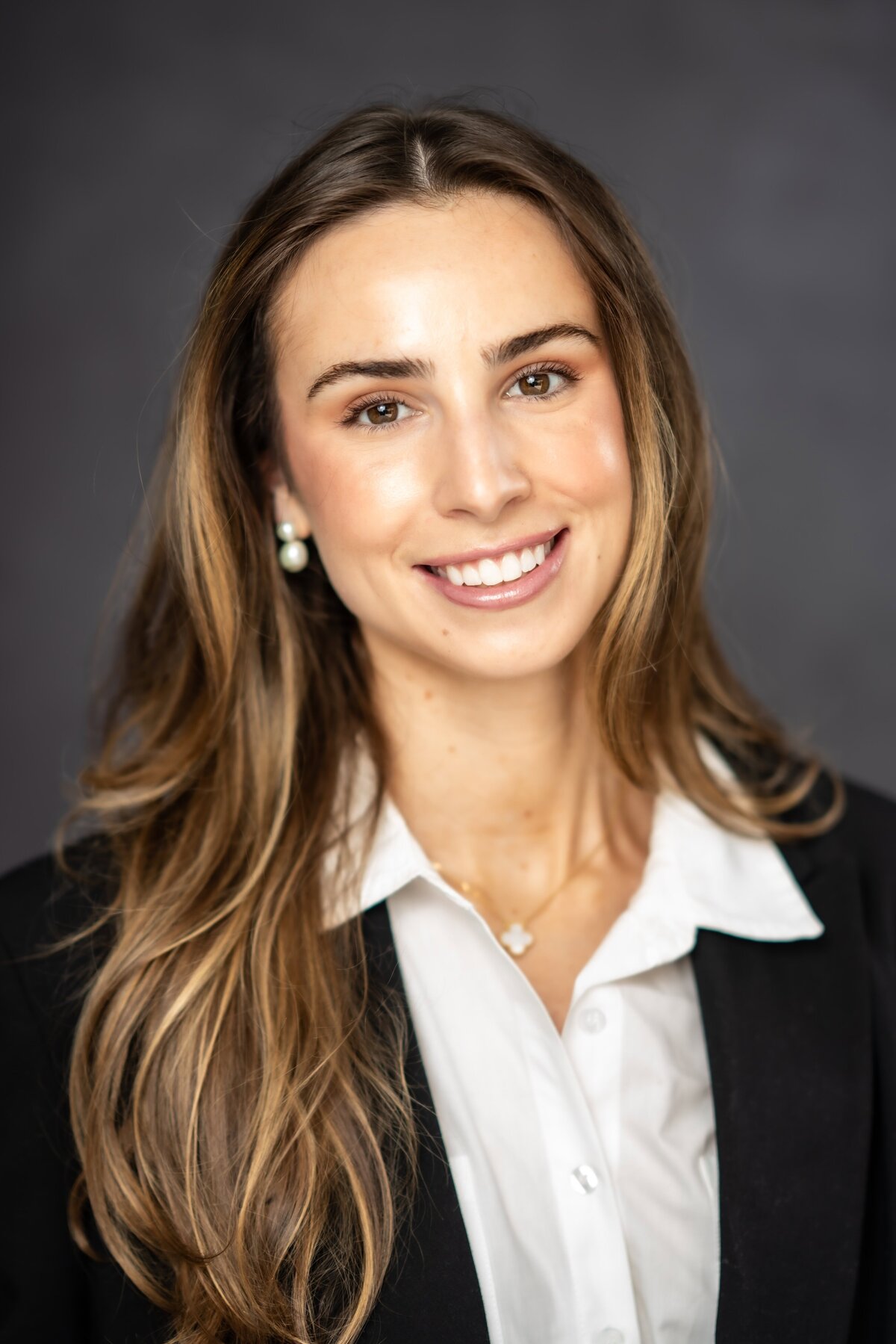 Portrait of a young woman with a bright smile and long hair in a dark blazer and a white shirt posing for a headshot