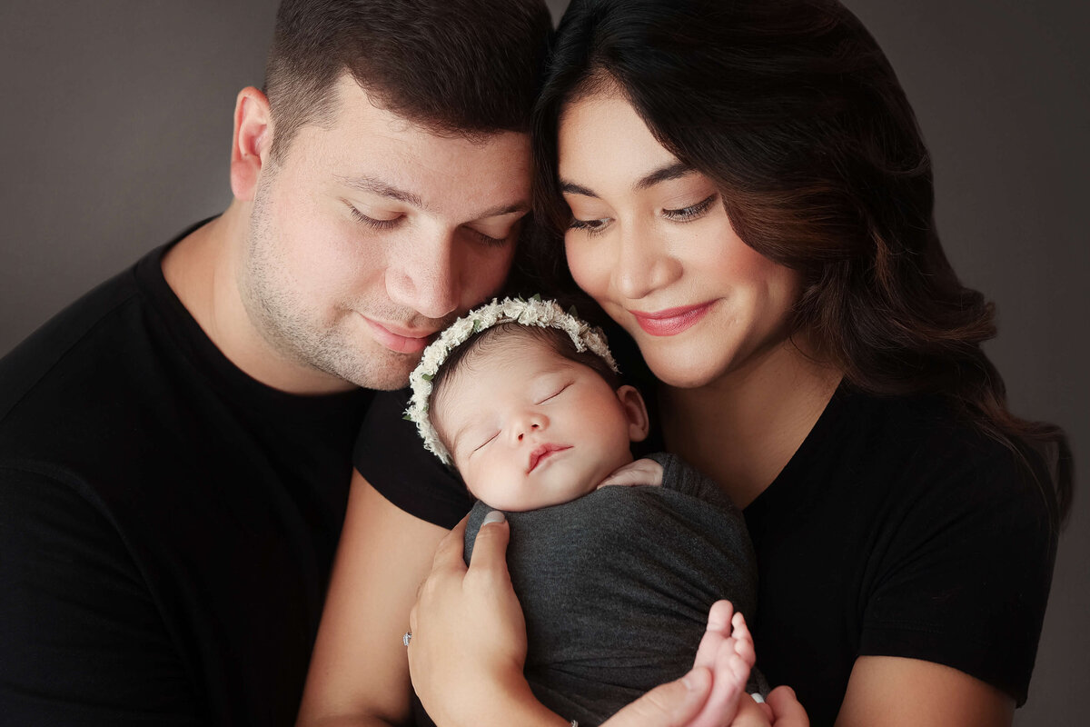 new parents with their eyes closed holding their newborn daughter in a newborn session