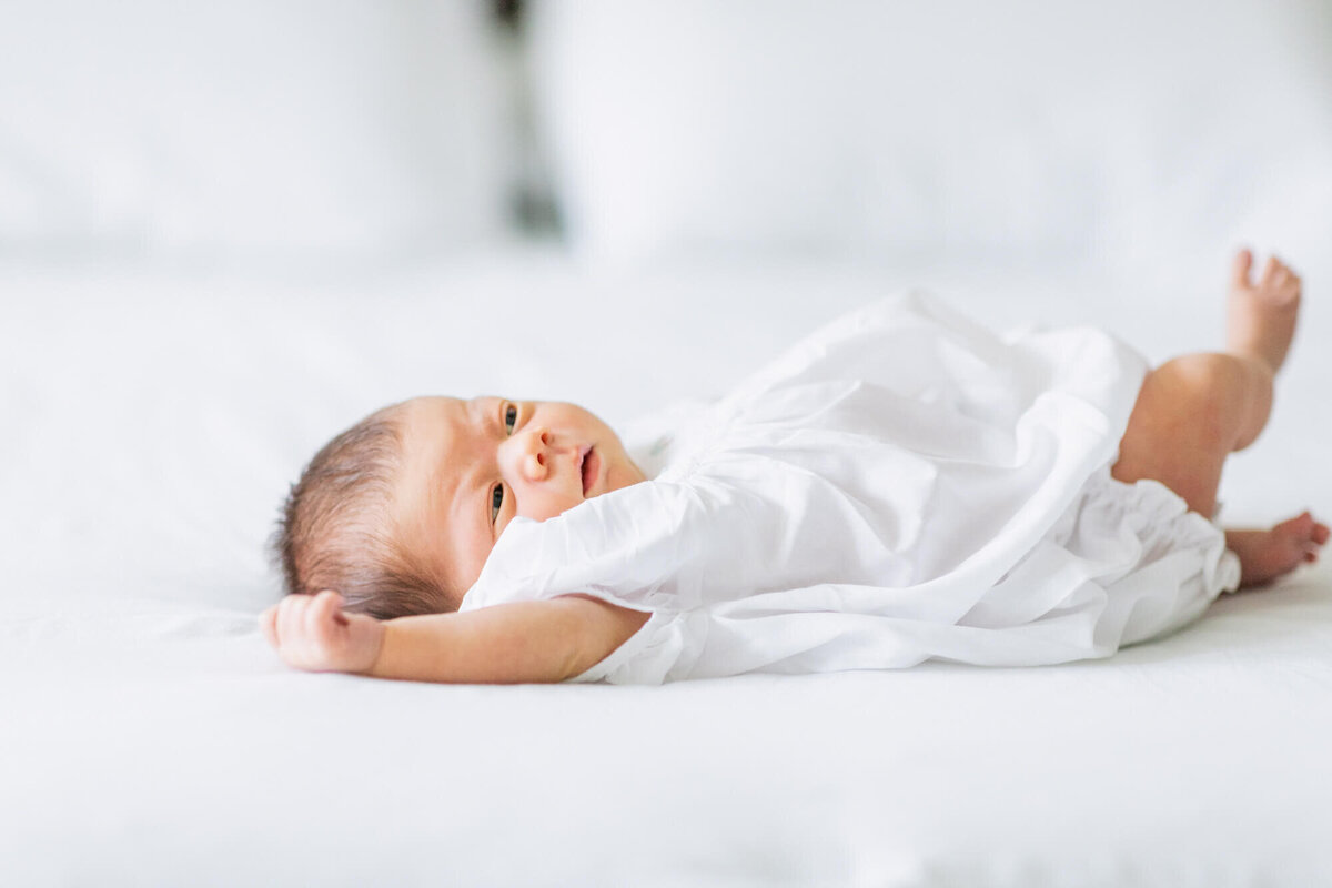 Newborn baby girl in a romper laying on a bed
