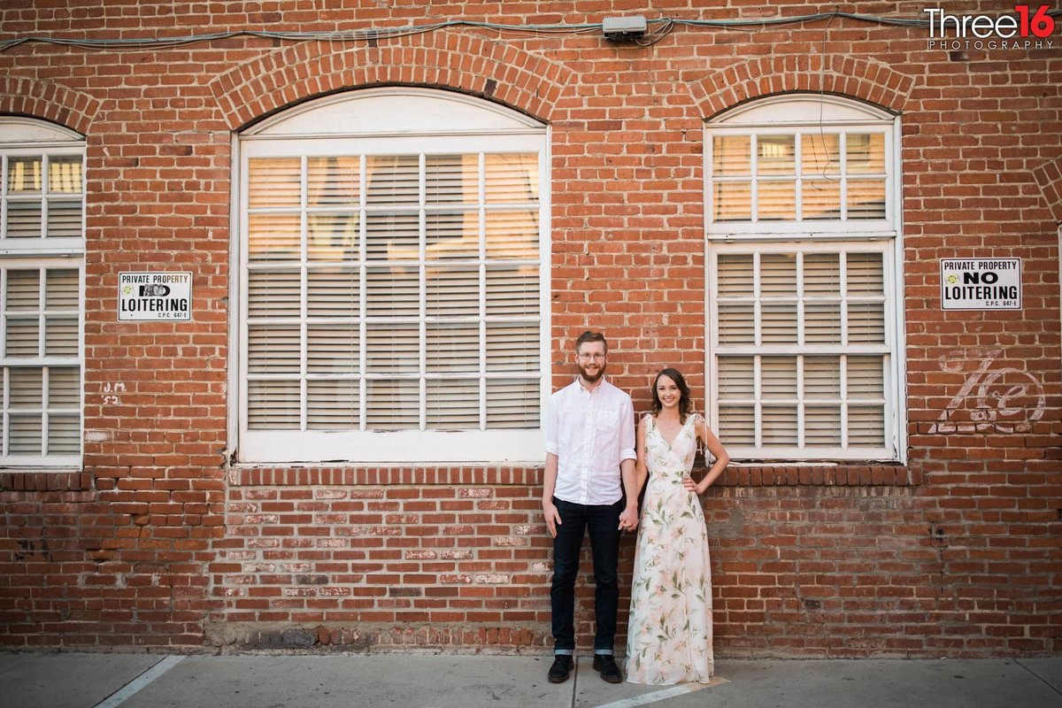 Engaged couple pose in front of an old brick building