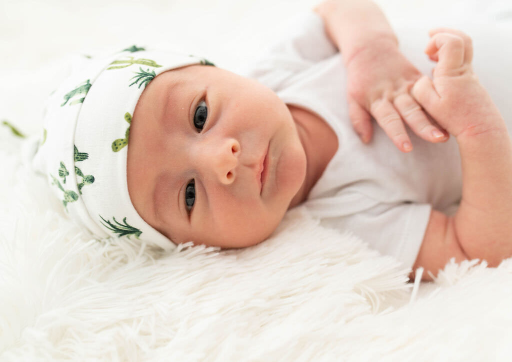 A newborn baby in a white and green hat.