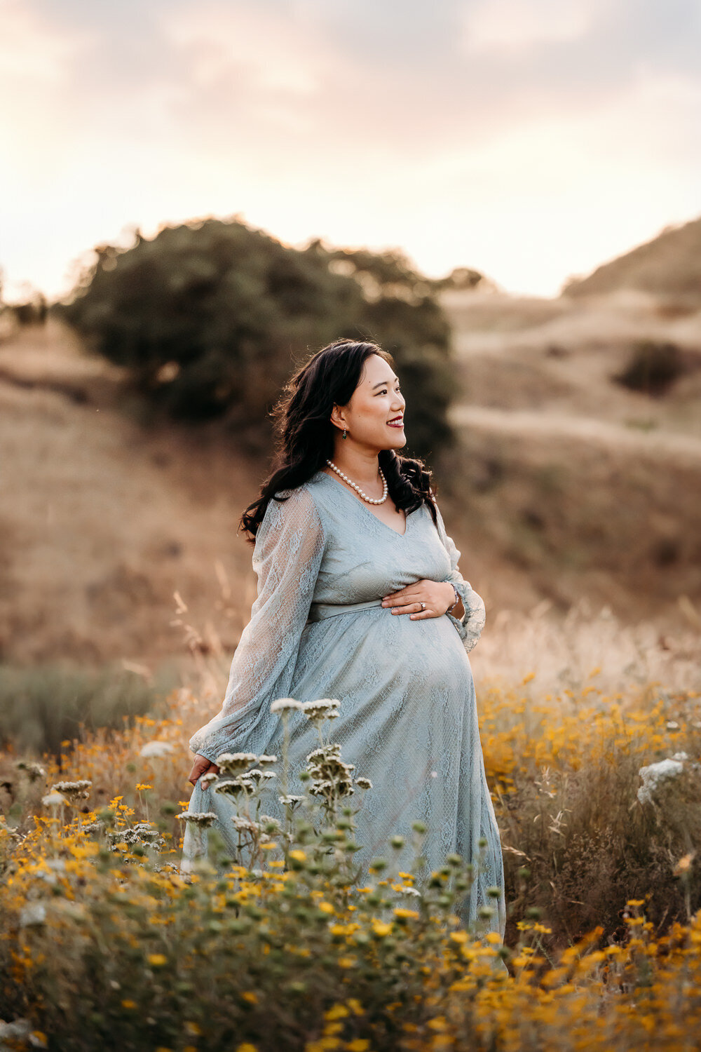 pregnant woman in blue maternity dress smiles looking off camera