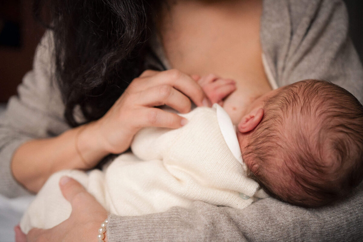 Close-up of a mother nursing her newborn, the baby held close in soft natural light.