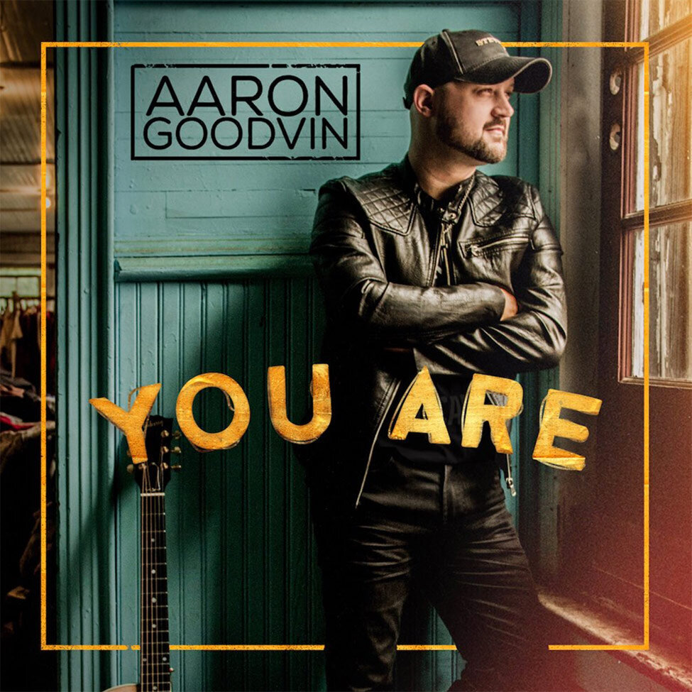 Single Cover Title You Are Artist Aaron Goodvin standing with arms crossed against his chest next to window green wall behind him