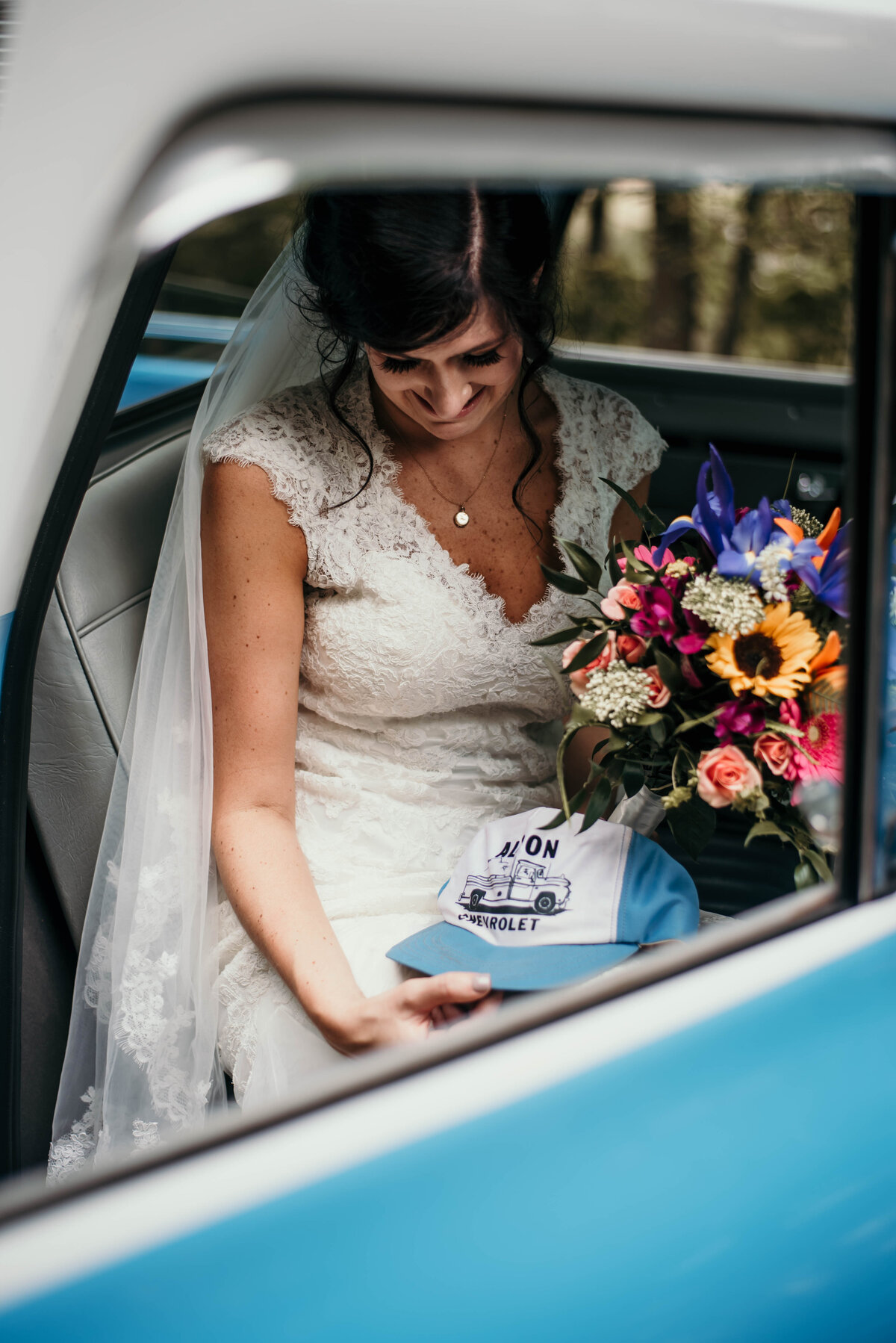 Bride sitting in car holding hat and bouquet