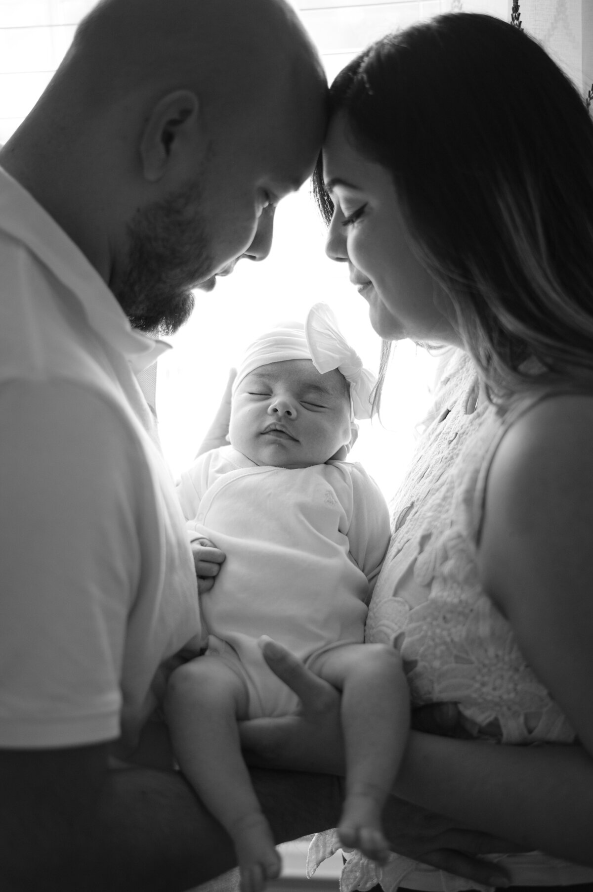 New parents hold their newborn baby girl while they lean into one another