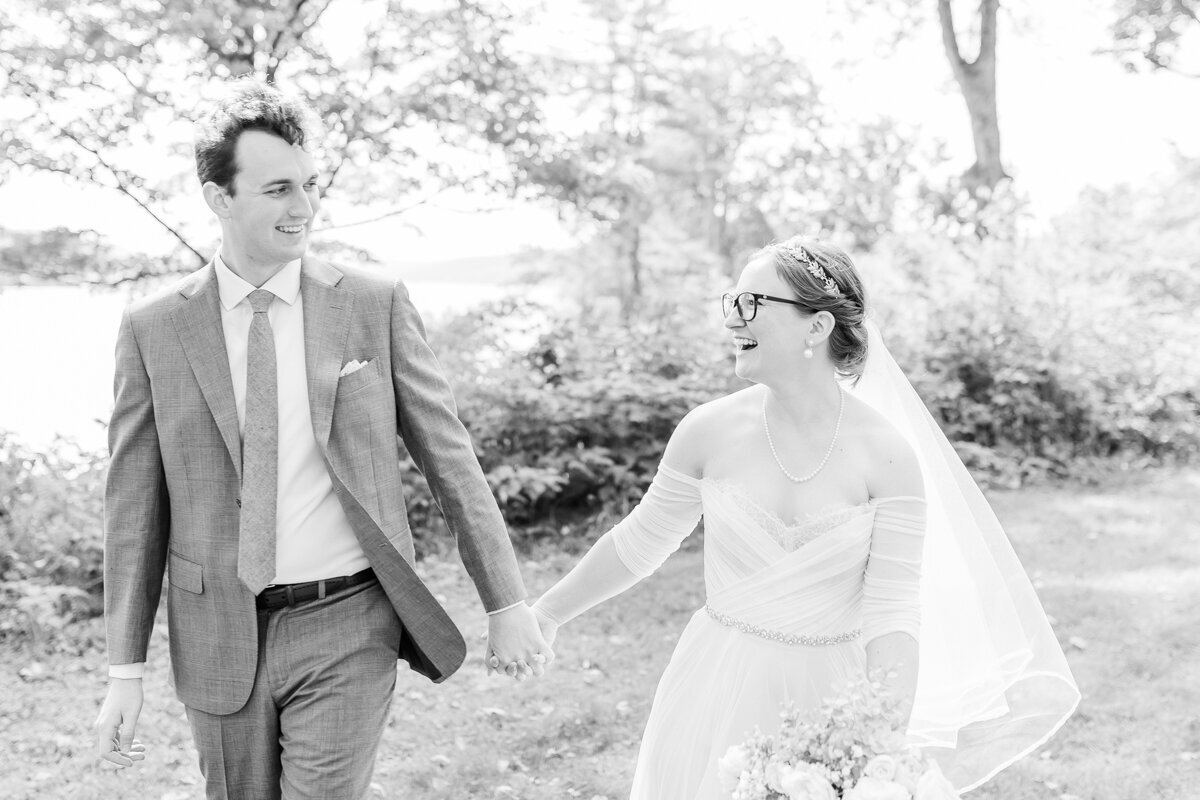 Black and white photograph of bride and groom walking holding hands while walking together at Glimmerglass State Park in Cooperstown, NY