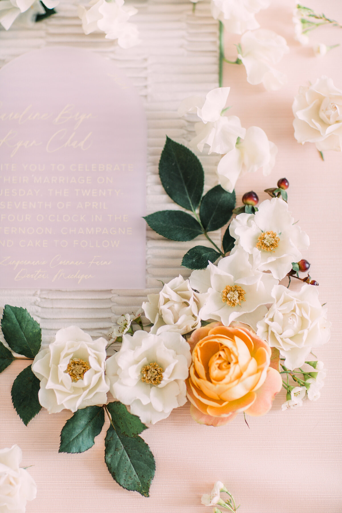 Closeup of styled wedding flatlay featuring frosted pink acrylic invitation and roses