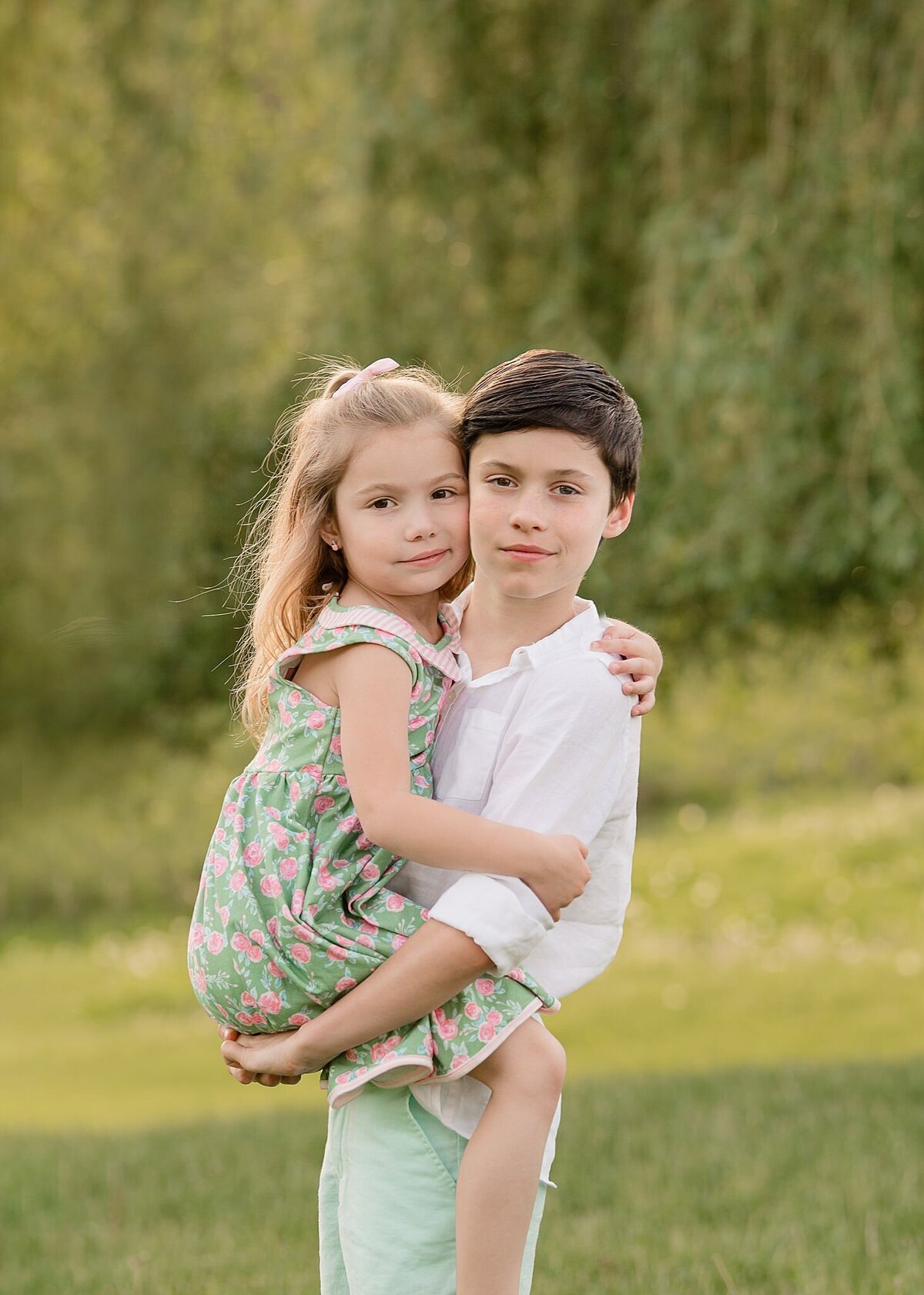 big brother holding little sister in floral dress