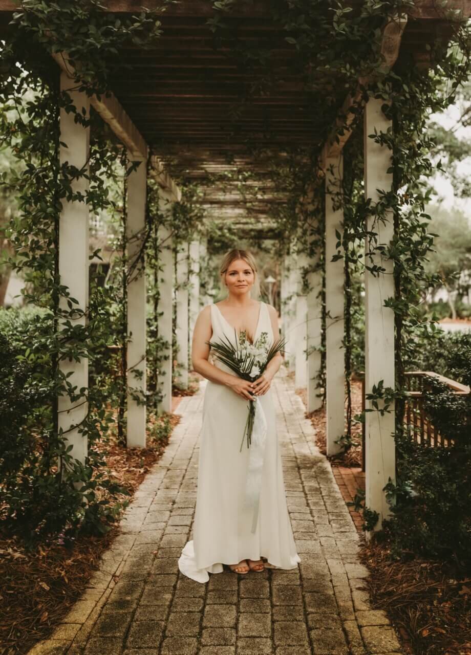young bride poses with tropical bouquet under garden arbor in rosemary beach