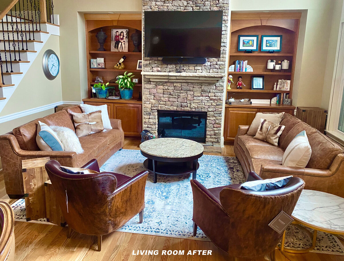 A cozy living room with a stone fireplace, a TV mounted above, and wooden shelves on either side. The room features brown leather sofas and chairs, a round coffee table on a patterned rug, and decorative items on the shelves.