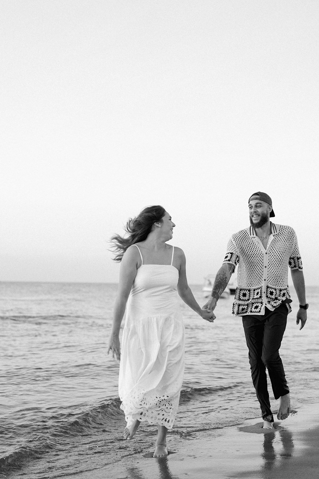 Black and white engagement photo of couple walking along the shore during New Buffalo Beach session
