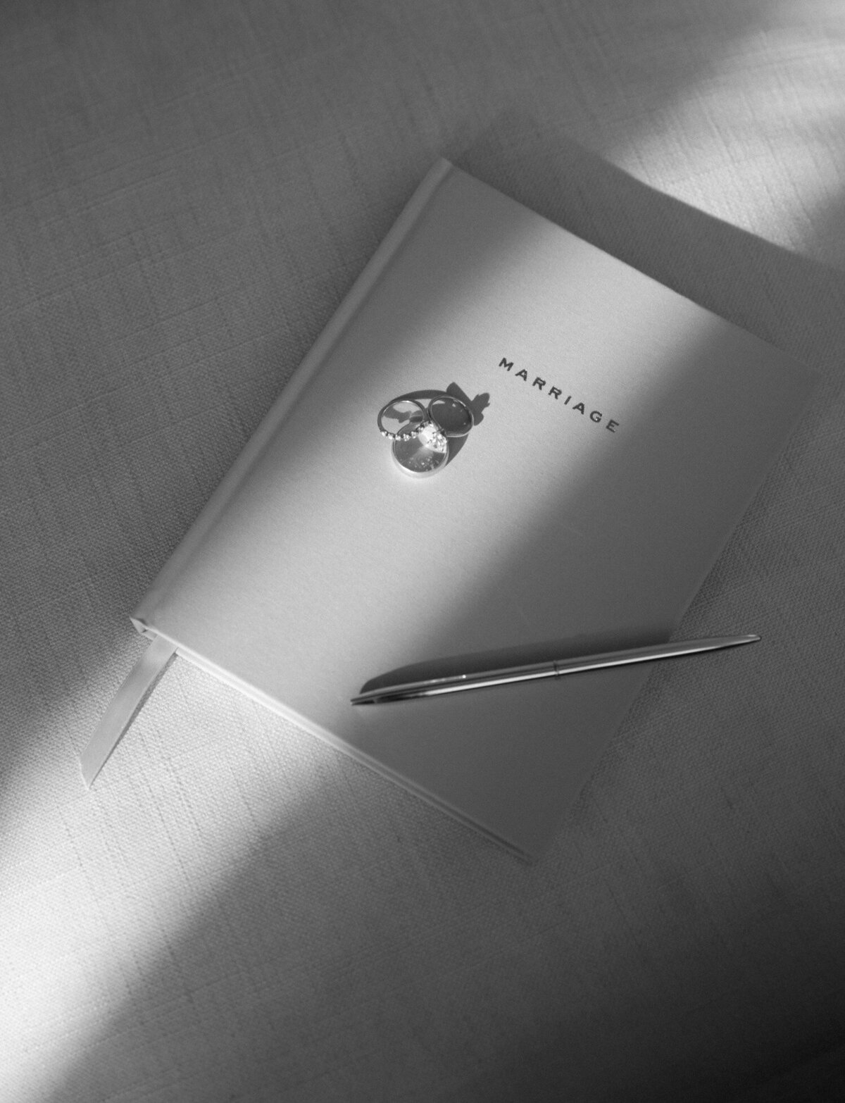directional light photography, film product photography of linen marriage journal with wedding rings, pen