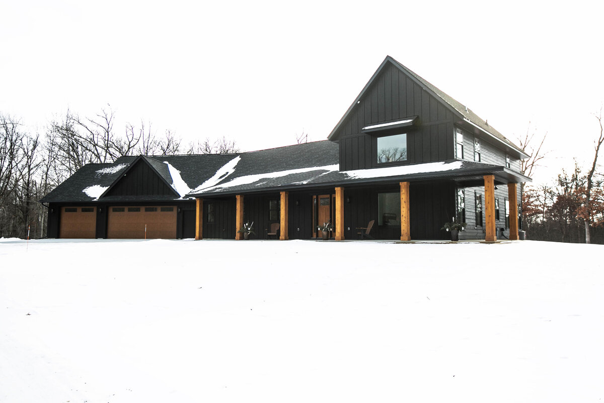 Exterior view of custom home in Elk River, Minnesota with black siding, wood details and front porch built by Cornerstone Custom Builds