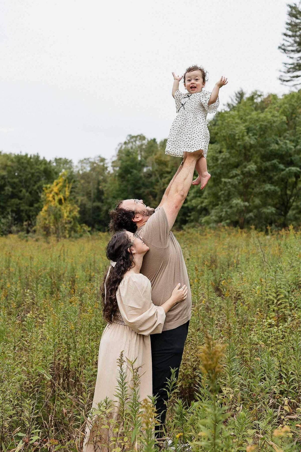 Dad lifting baby daughter into the air while mom looks on. Cleveland family photography in a field.