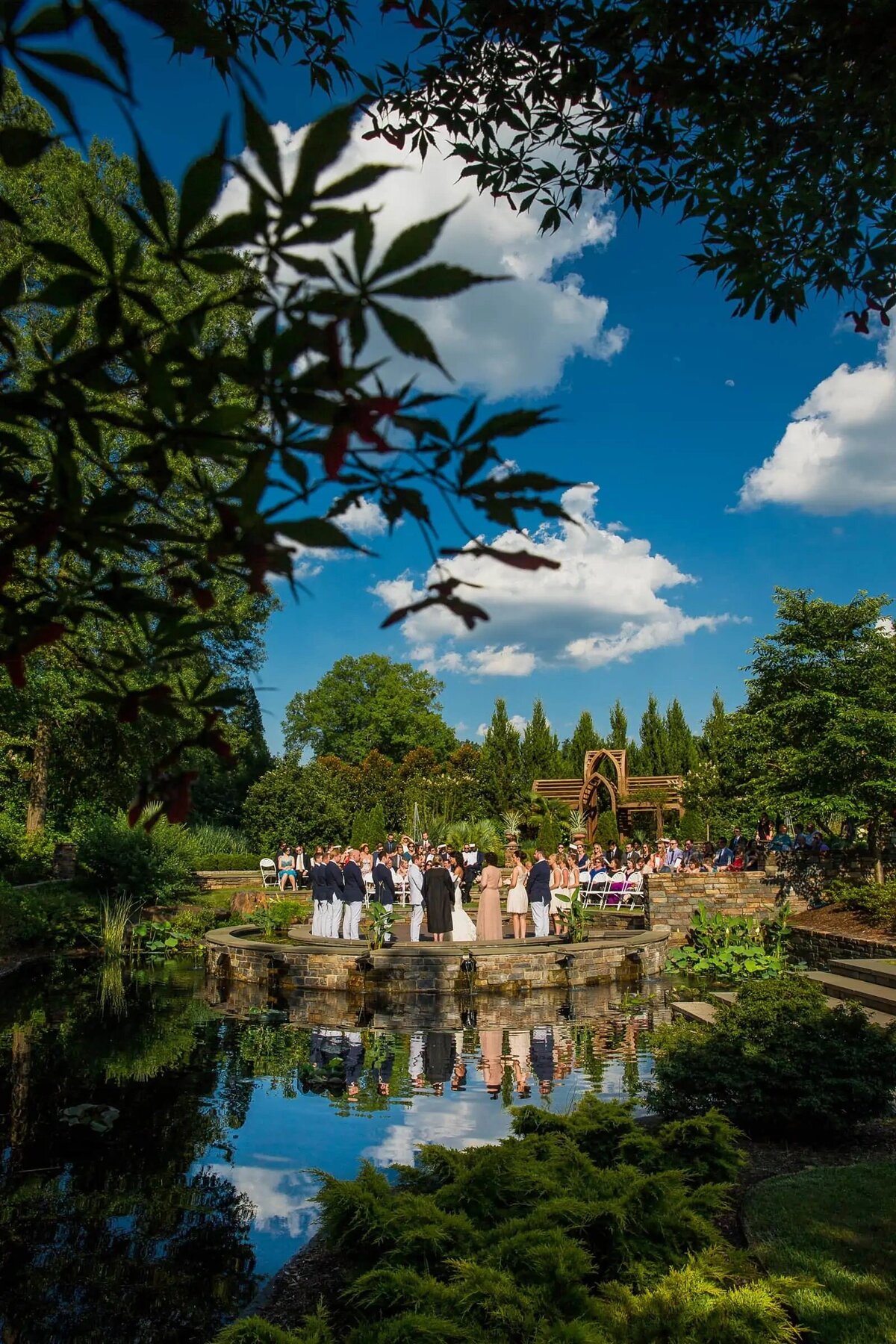A wedding by a serene pond at Duke Gardens, the tranquil water reflecting the clear blue sky above