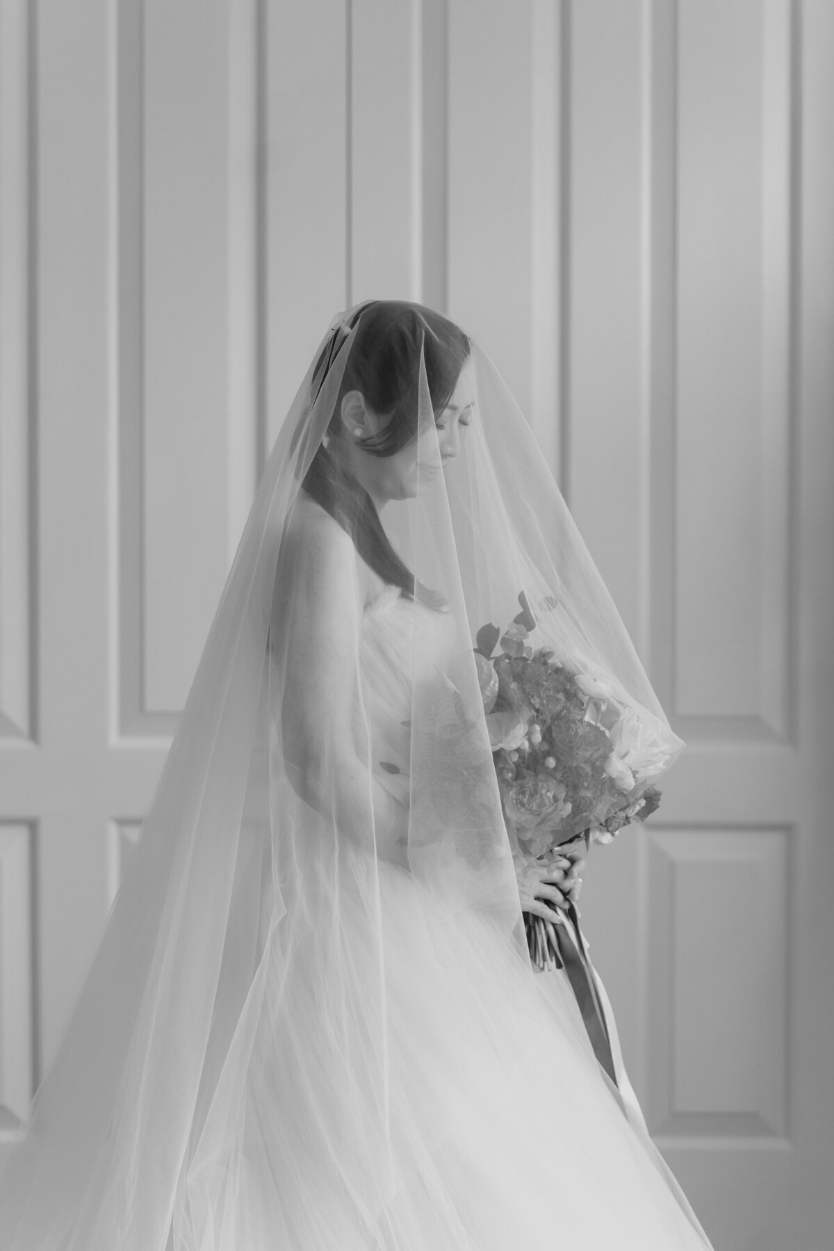 bride wearing her veil looking down at her bouquet