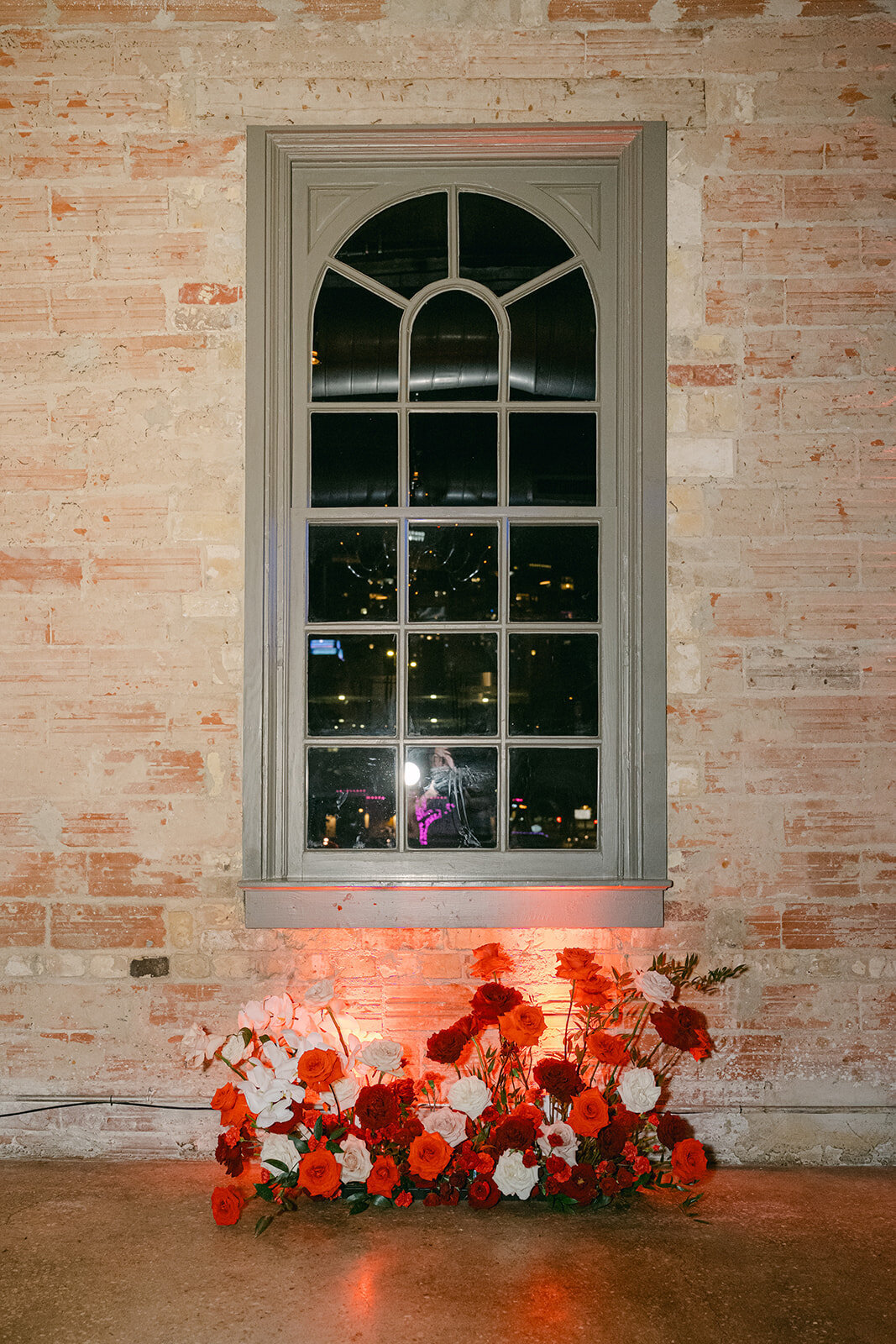 Architectural window with evening light and delicate red florals in downtown San Antonio wedding
