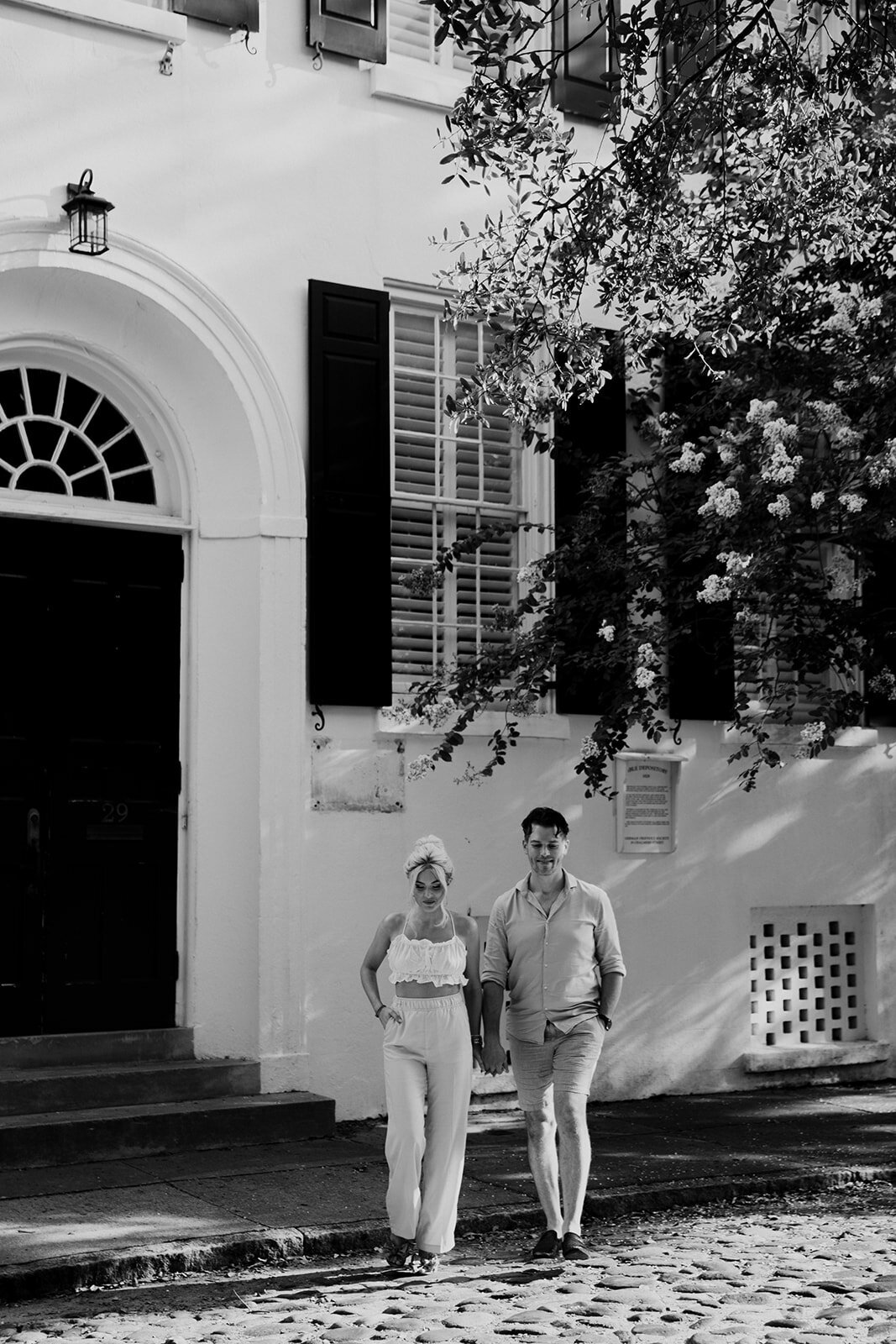 Couple walking on cobblestone in front of white house with black door