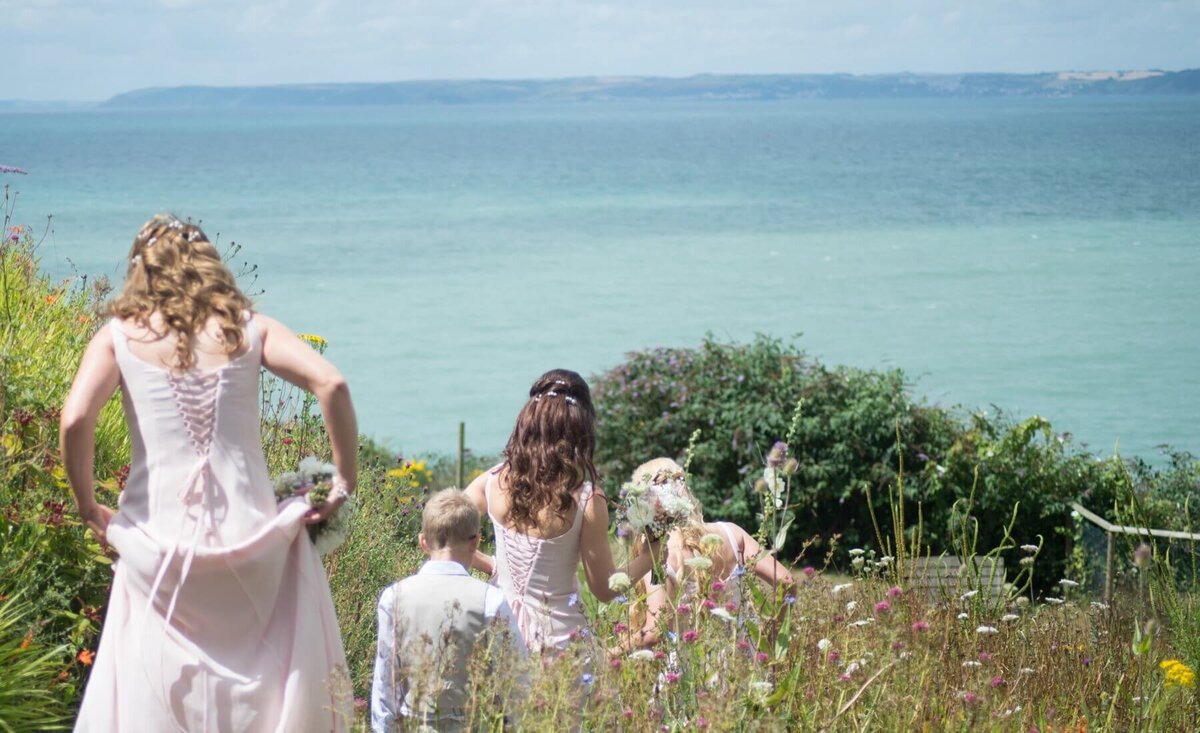 A group of bridesmaids walking down the hill towards the beach holding up their dresses