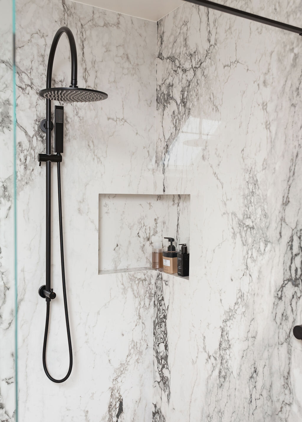 A modern white and grey marble glass-enclosed shower with matte black hardware.