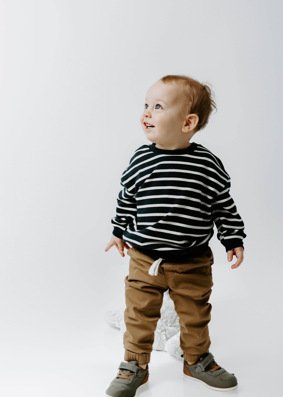 A baby boy in a striped sweater and pants captured by a Pittsburgh family photographer.
