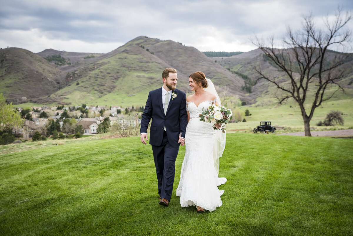 A bride and groom smile at each other and walk hand-in-hand toward the camera at The Manor House in Littleton, Colorado.