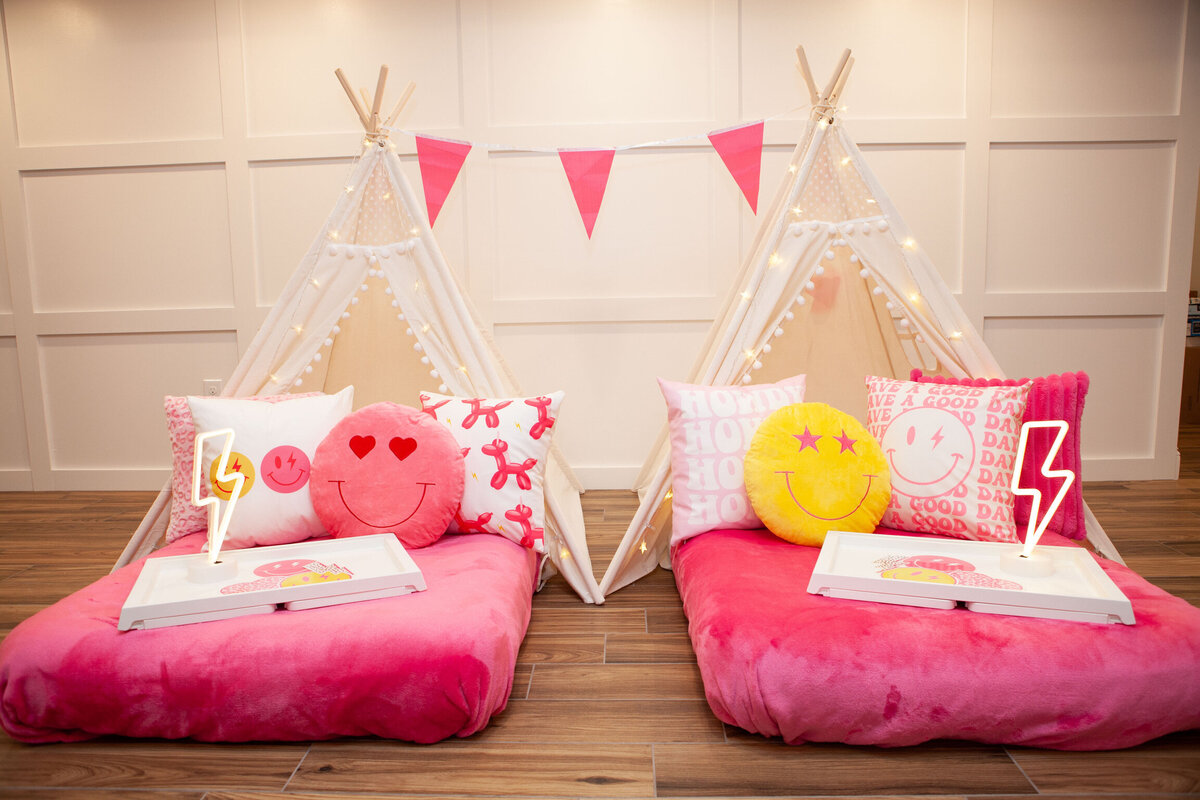 two pink teepee beds with smiley face pillows and preppy props