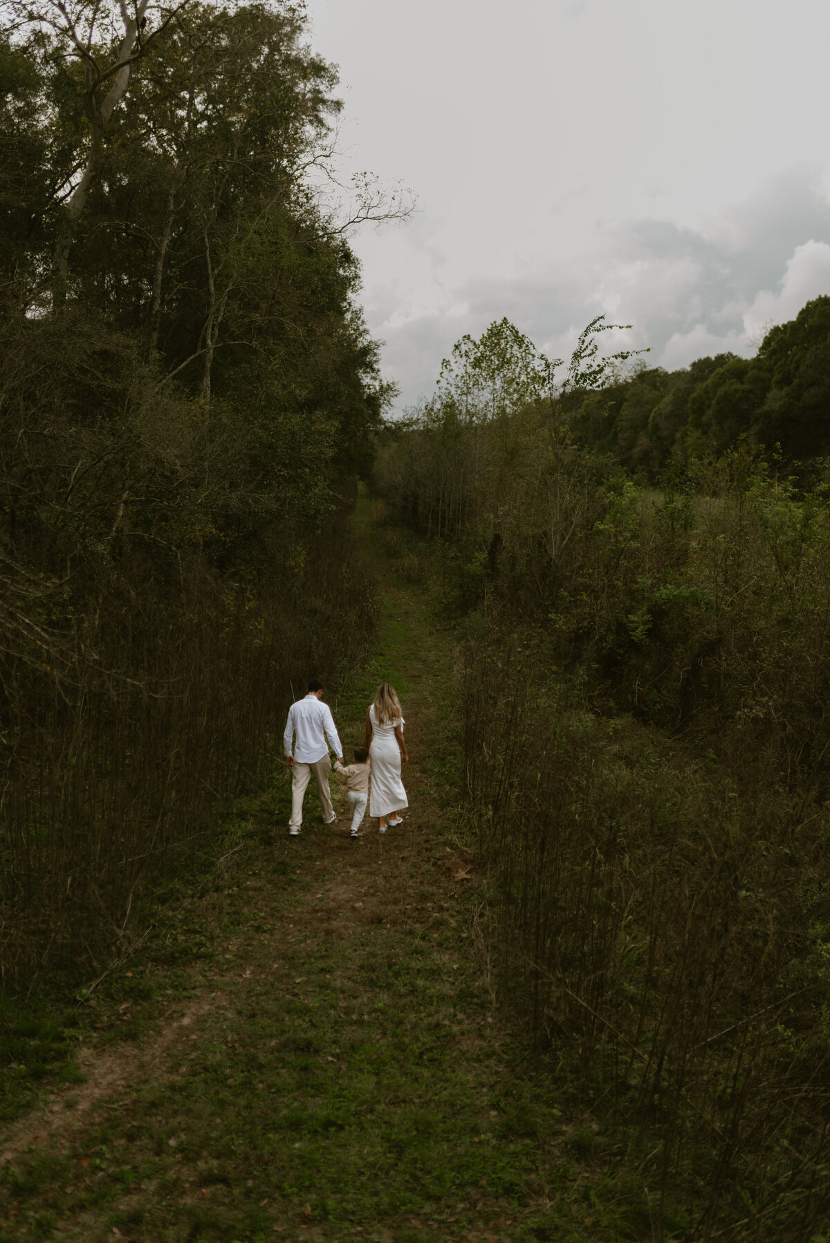 a family of three walking in lush green fields holding hands