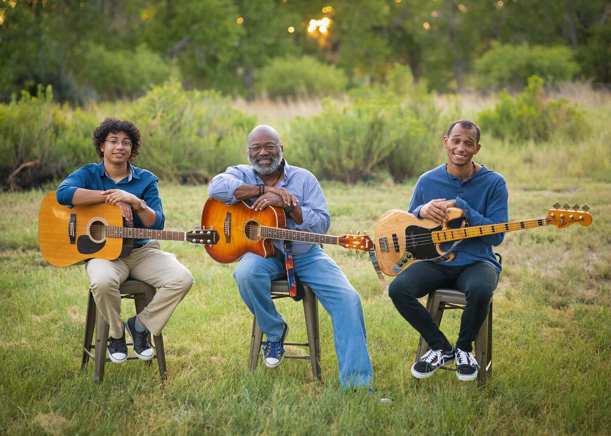 a father and his two sons sitting in a field playing guitar