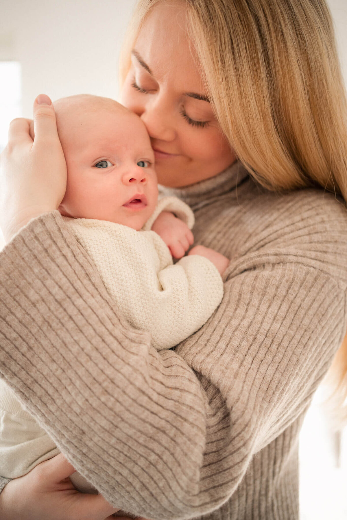 Mother in a ribbed sweater holding her baby close, gently kissing their cheek.