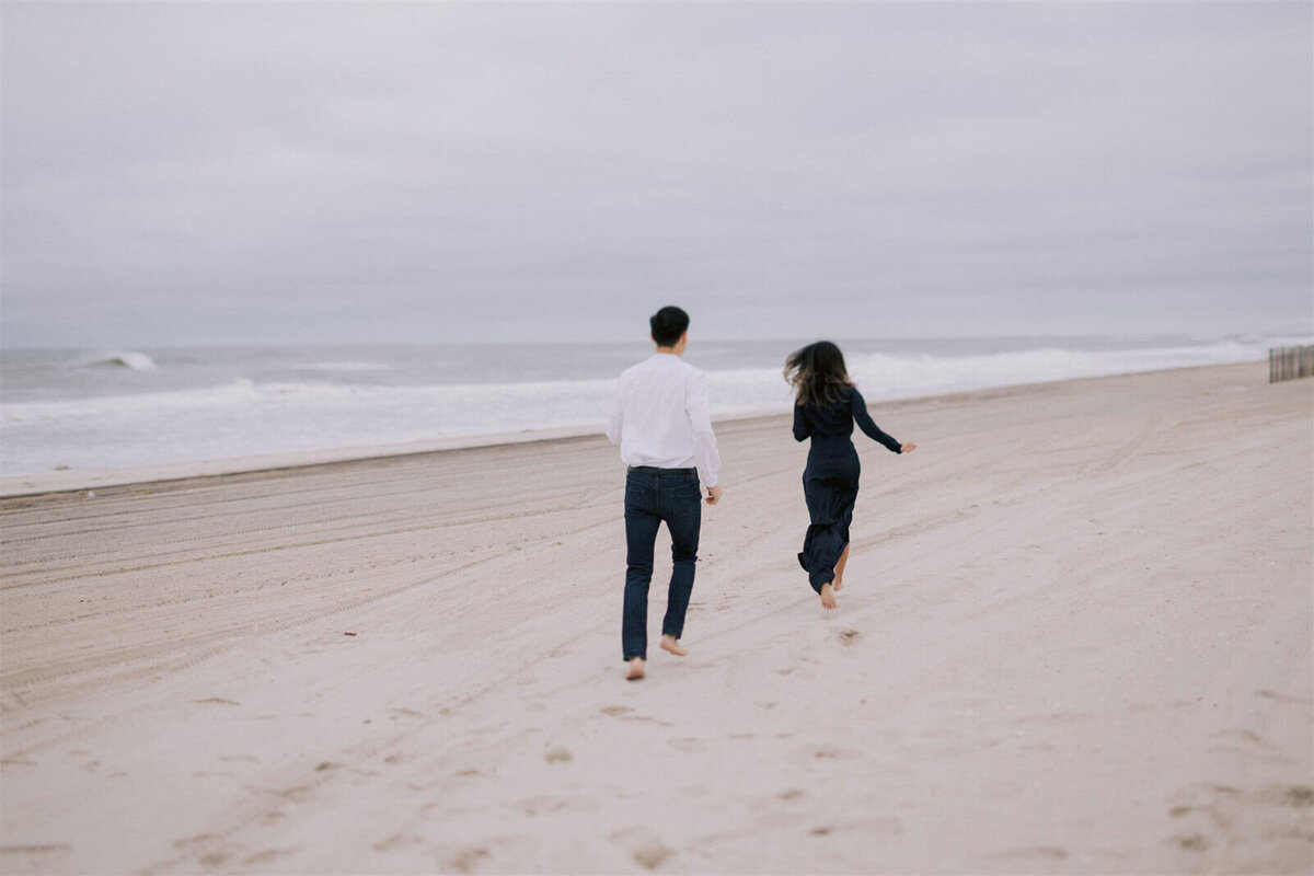 The engaged couple is running along the shore in Fire Island Beach, NY. Engagement Image by Jenny Fu Studio
