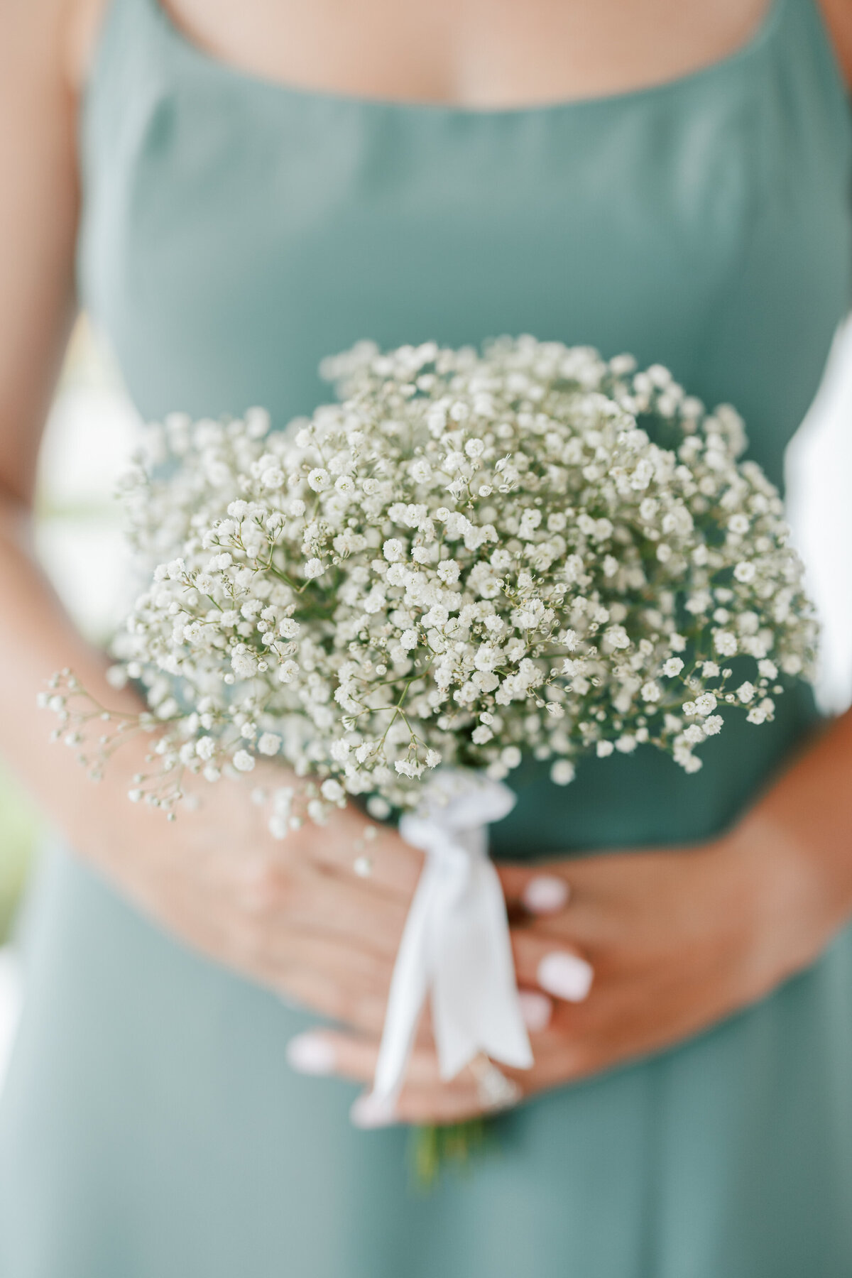 Close-up of bridesmaid holding baby's breath bouquet tied with white ribbon at Cancun wedding.