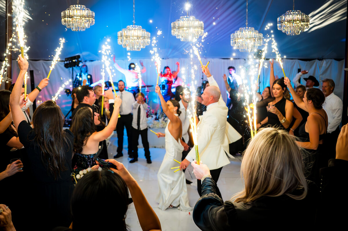 A bride and groom dance surrounded by wedding guests who are all holding fireworks.