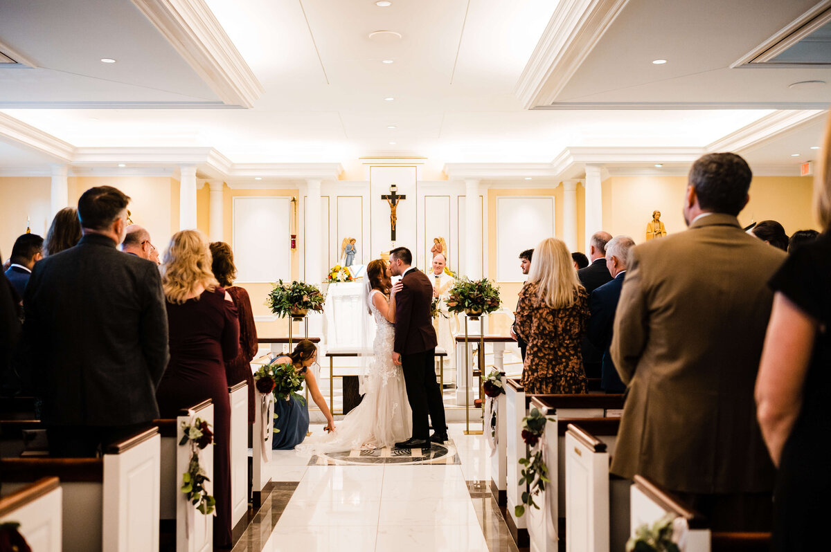 Church wedding photographed by Charlottesville wedding photographer with bride and groom at the altar kissing at the end of their ceremony with a wooden cross behind them
