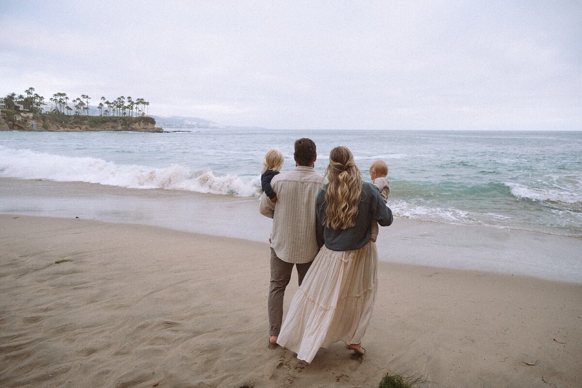 family of four wearing neutrals walking near ocean at crescent bay beach