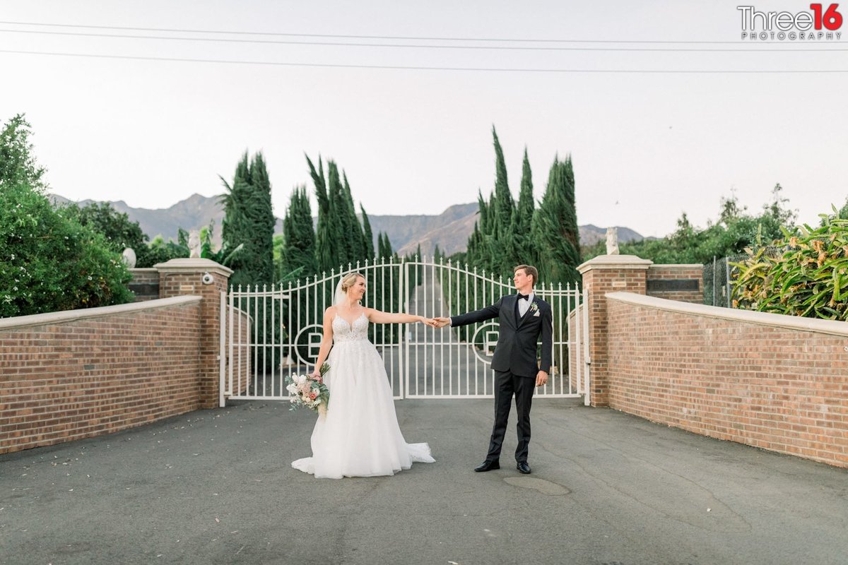 Bride and Groom pose on the Bella Vista Groves driveway with white gate behind them
