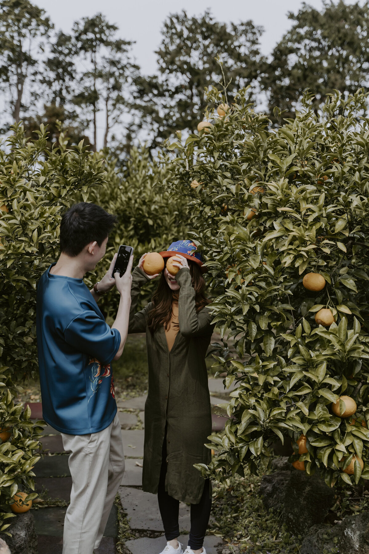 the groom taking picture of the bride doing silly pose with tangerines