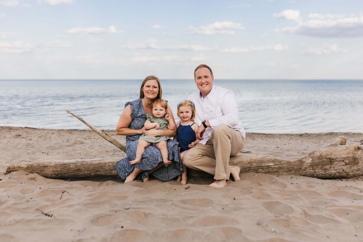family posing on a beach while sitting on a piece of driftwood