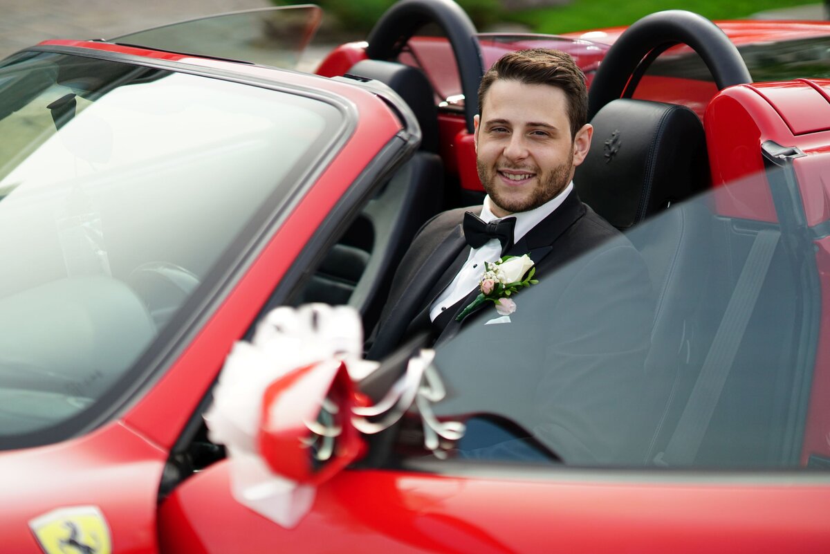 The groom sits confidently in the driver’s seat of a sleek red Ferrari, showcasing a stylish and high-energy moment. This image highlights the groom's sophistication and adds a touch of luxury and excitement to his wedding portraits.